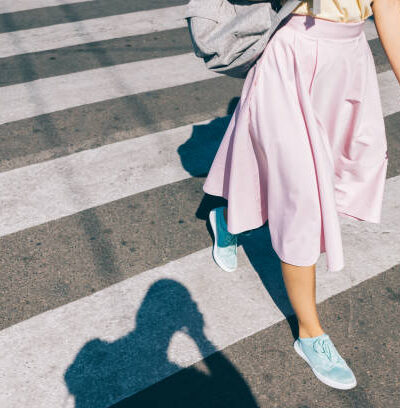 Young woman in a pink skirt and sneakers crossing the road in the summer