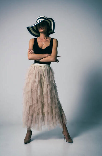 Stylish energetic woman in a black dress poses hiding her face with a hat